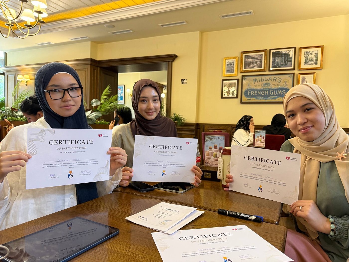 Three participants holding their certificates of participation at a cafe