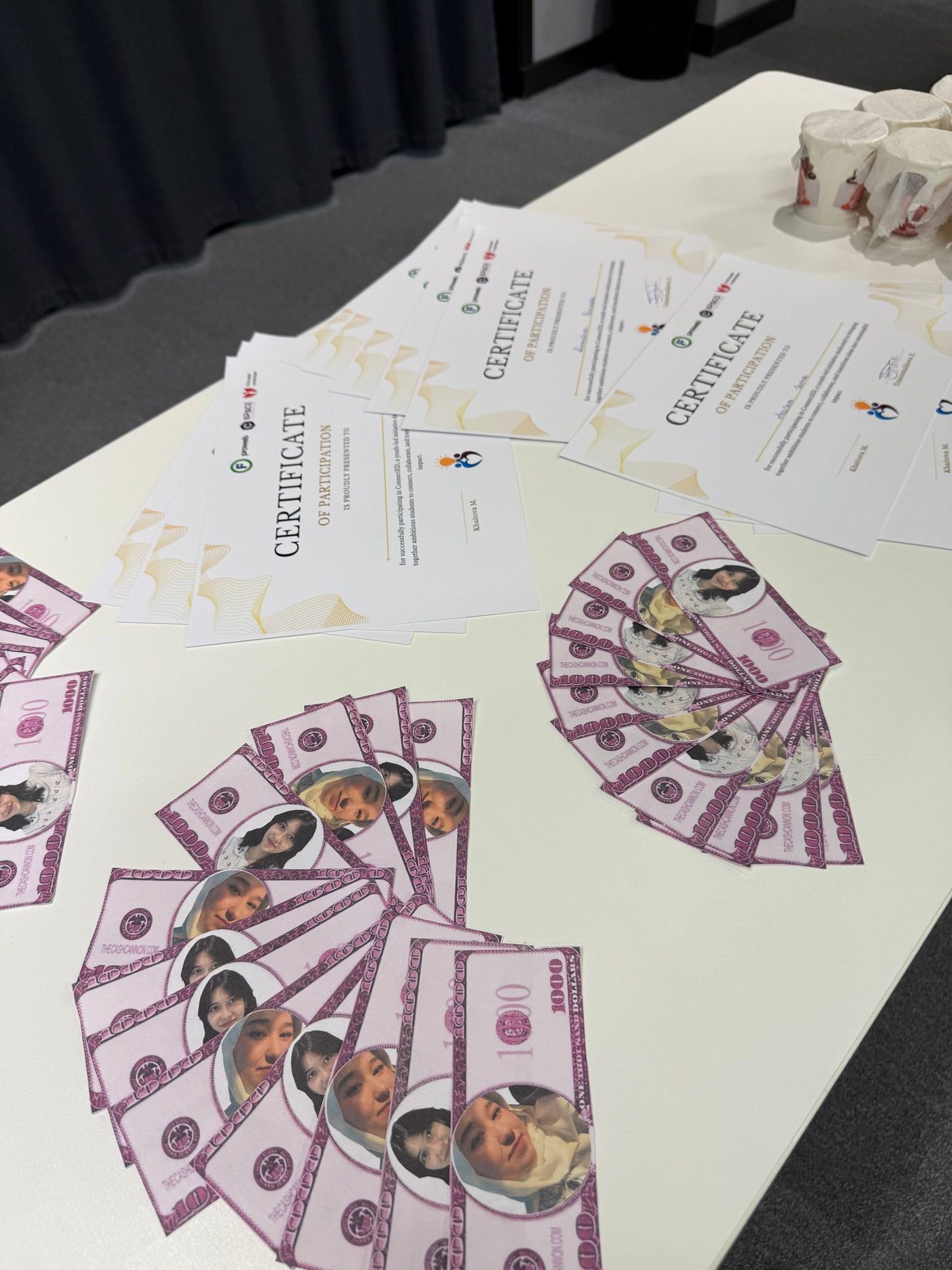 Certificates and play-money bills with participants' photos laid out on a table