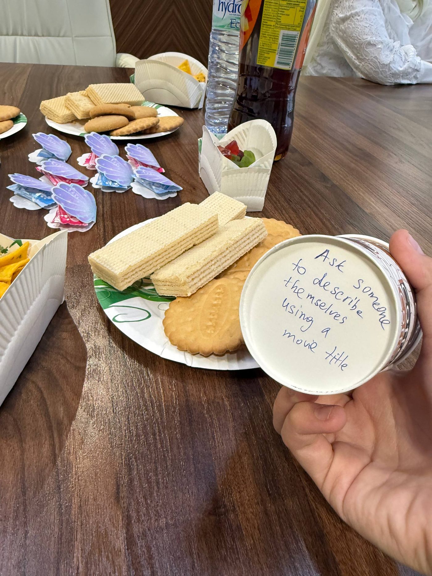 A snack table with an icebreaker prompt written on a paper cup: ask someone to describe themselves using a movie title